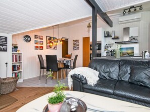 A modern living room with a black leather sofa, a dining area with a table and chairs, and a kitchen with a white countertop and various appliances.