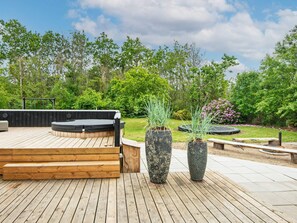 A wooden deck with a hot tub, stone planters, and a garden with trees and shrubs.