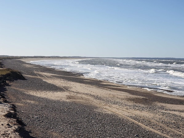 A beach with pebbles and sand, waves crashing, and a clear sky.