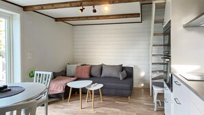 A modern kitchen with white cabinets, a dining area with a white table and chairs, a grey sofa with cushions, and a wooden floor. - 4 Person Holiday Home in Farjestaden (Farjestaden)