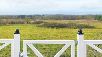 A white fence with a gate, a grassy field, and a distant view of trees and a body of water.