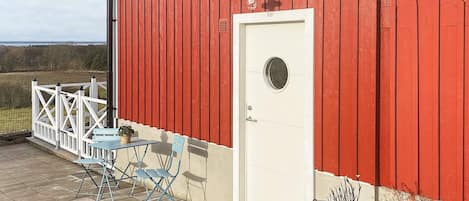 A red barn with a white door, a small patio with a table and chairs, and a white fence.