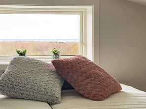 Una cama con tres almohadas y vista a un bosque a través de una ventana.