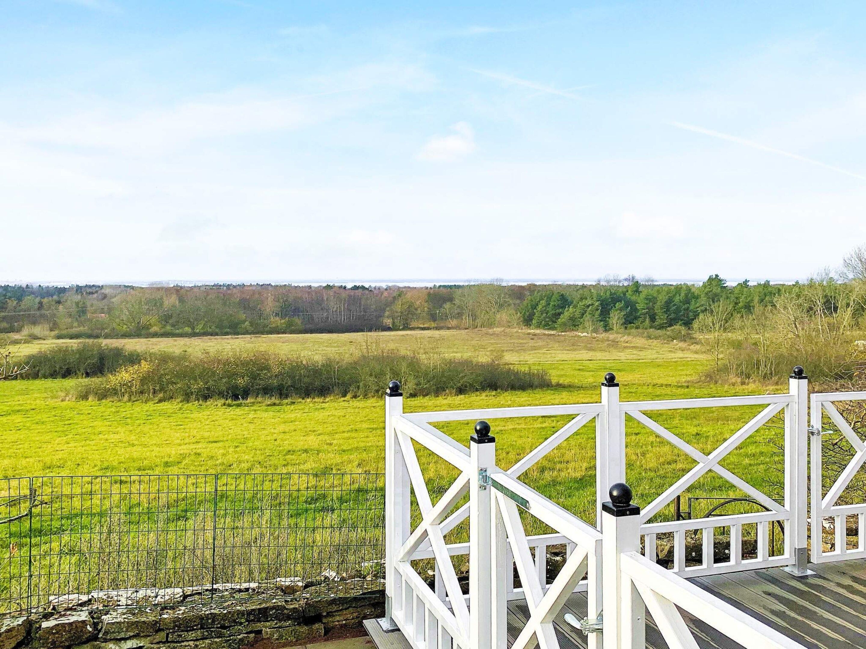 A white wooden deck with a metal railing overlooking a green field.