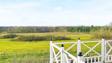 A white wooden deck with a metal railing overlooking a green field.