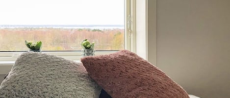 Un lit avec trois oreillers et une vue sur une forêt, visible par la fenêtre.