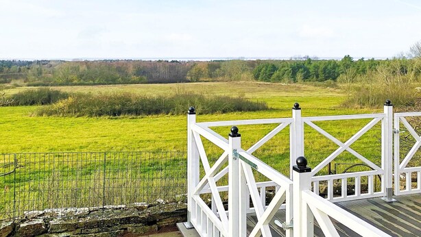 A white wooden deck with a metal railing overlooking a green field. - 4 Person Holiday Home in Farjestaden (Farjestaden)