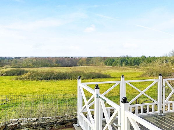 Una terraza de madera blanca con barandilla metálica que da a un campo verde.