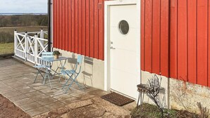 A red barn with a white door, a small patio with a table and chairs, and a white fence. - 4 Person Holiday Home in Farjestaden (Farjestaden)
