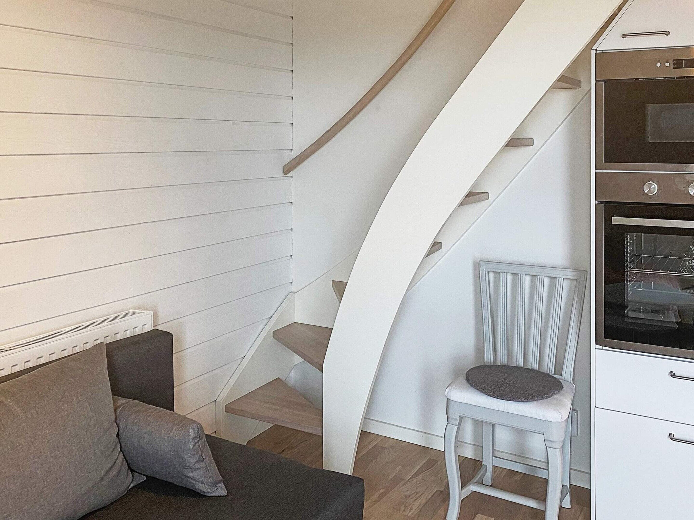 A modern kitchen with a built-in oven, a white cabinet, and a staircase with a white chair.