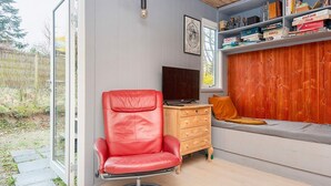 Una habitación moderna con una butaca de cuero rojo, un aparador de madera, un televisor y una estantería.