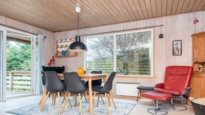 Una cocina moderna con armarios de madera, una mesa de comedor con sillas, una silla roja y un ventanal con vistas a árboles.