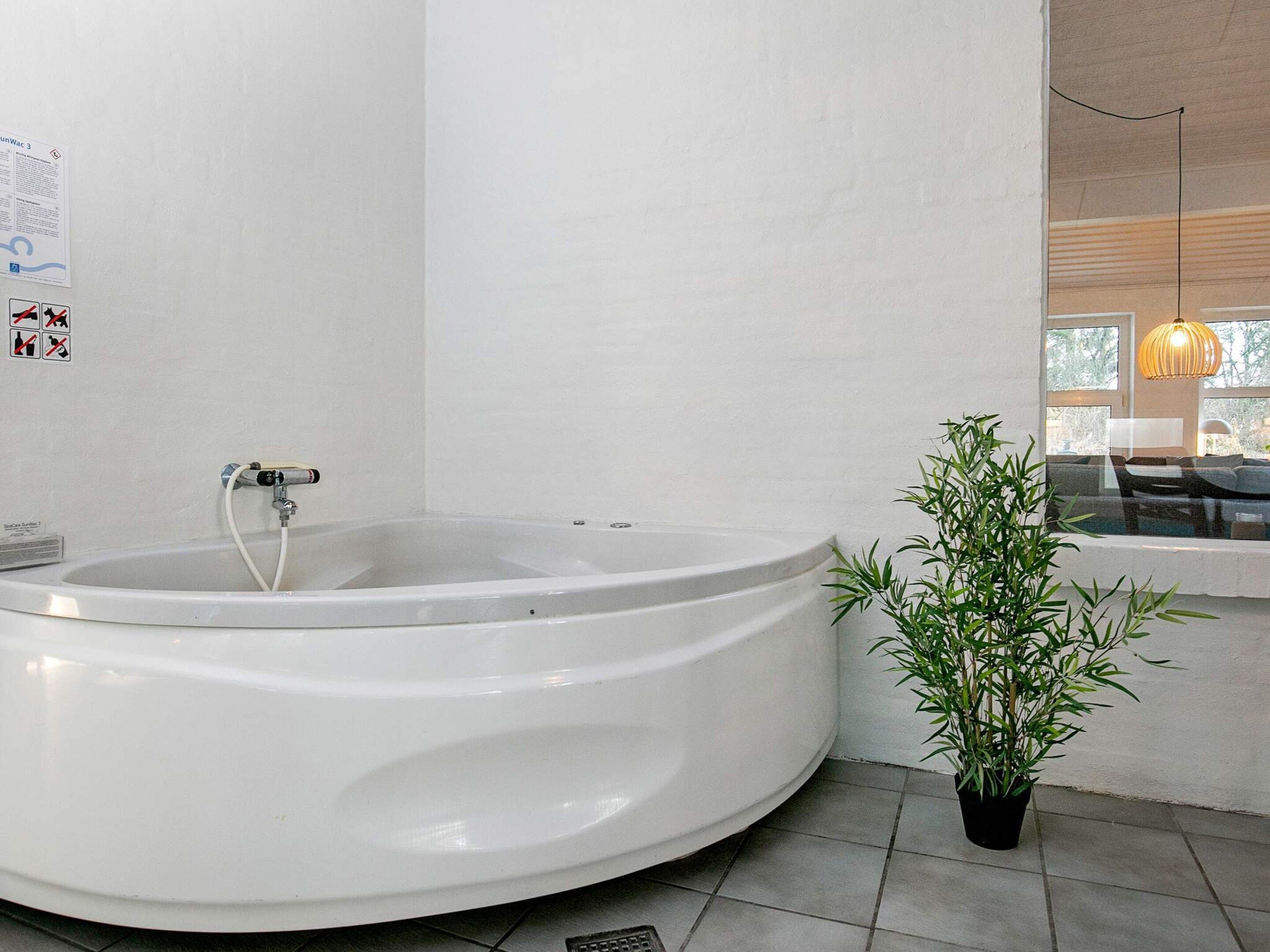 A modern bathroom with a large bathtub, a potted plant, and a window with a view of the outdoors.