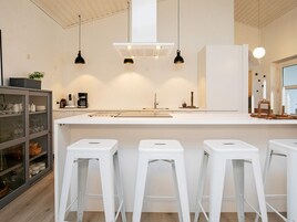 Una cocina moderna con encimeras blancas, una isla central y tres taburetes blancos.