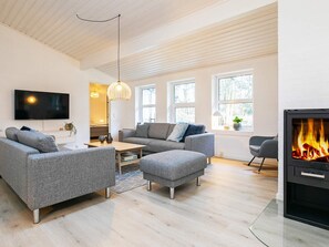 A modern living room with a fireplace, grey sofas, a flat-screen TV, and large windows.