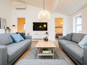 Uma sala de estar moderna com dois sofás cinza, uma mesa de centro de madeira e uma grande TV de tela plana na parede.