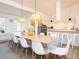 Una cocina moderna con una mesa de madera, sillas blancas, lámparas de mimbre colgantes y un reloj a la vista.
