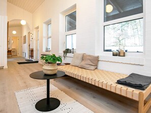 A modern interior with a wooden bench, a round table with a woven basket, and large windows with a view of trees.