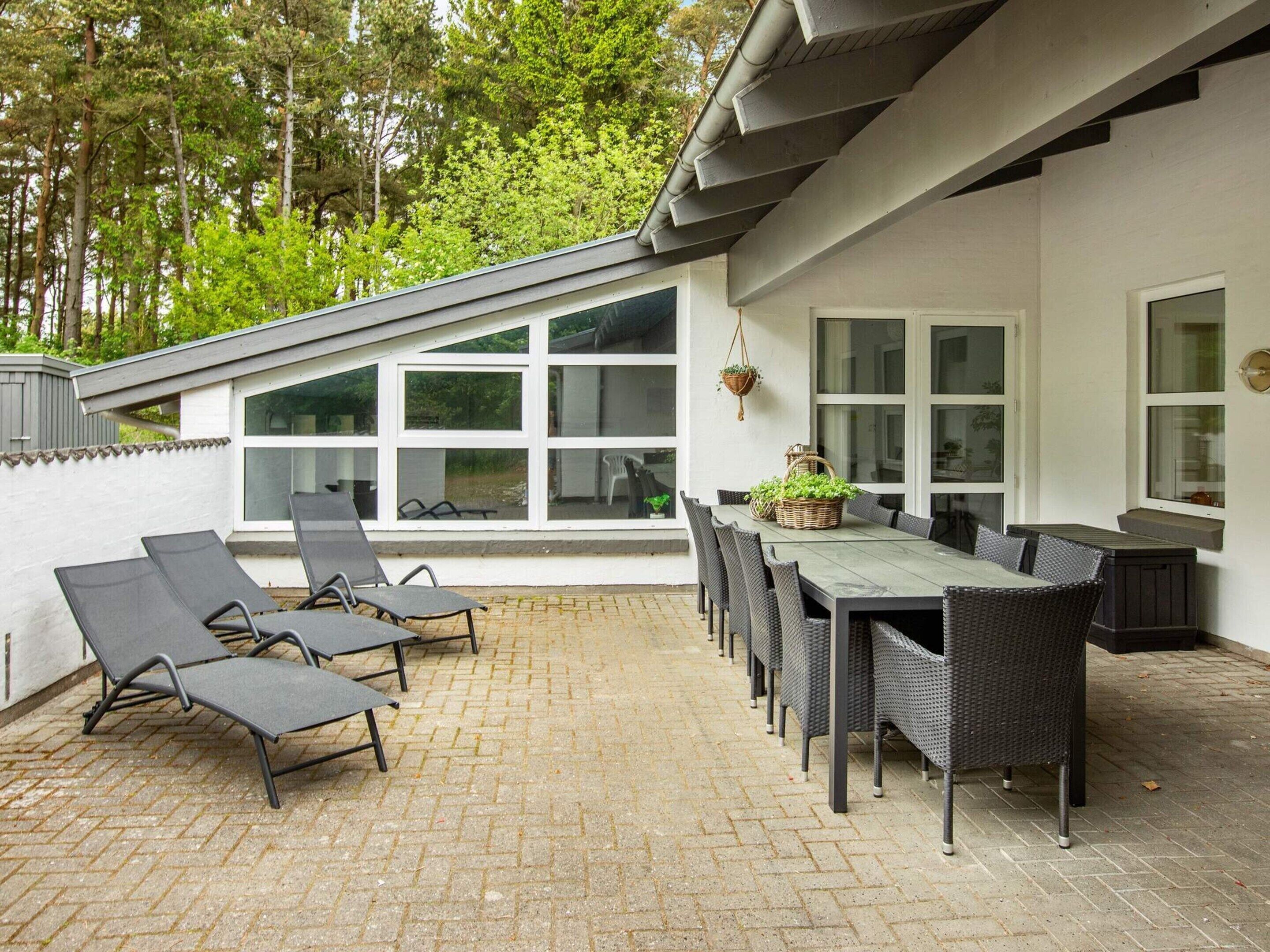 Een terras buiten met een eettafel en stoelen, een zonneliggedecke en een hangplant.