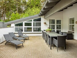 Un patio al aire libre con mesa y sillas, un espacio para tomar el sol y una planta colgante.
