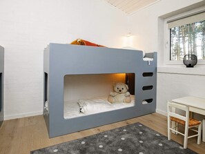 A bunk bed with a teddy bear, a small table, and a window with a view of trees.