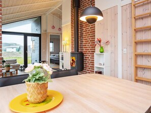 A modern interior with a wooden dining table, a sofa, a fireplace, and a large window. - 5 Star Holiday Home in Lokken (Lokken)