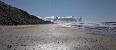 A beach with a clear sky, a visible rainbow, and footprints on the sand.