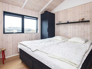 A bedroom with a bed, a window, a shelf with decorative items, and a red stool. - 5 Star Holiday Home in Lokken (Lokken)
