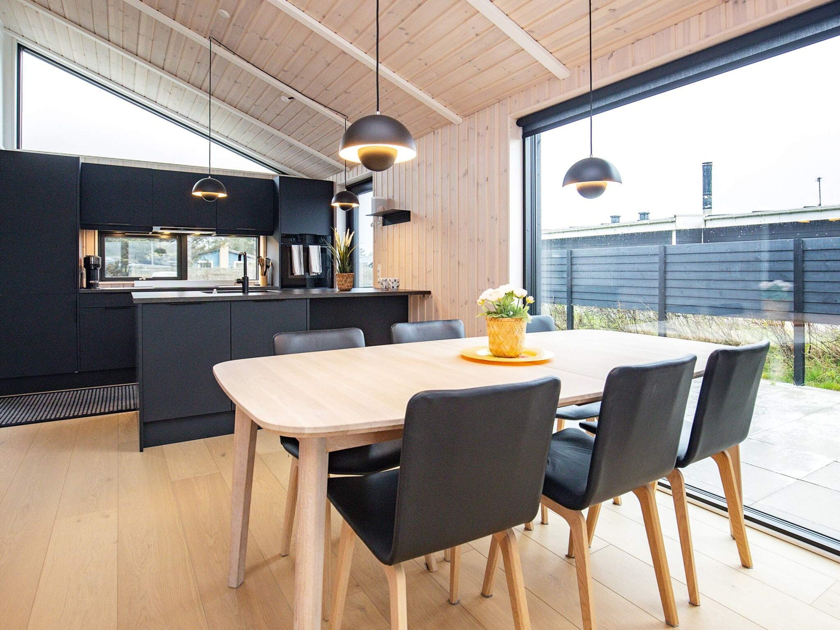 Une cuisine moderne avec des meubles de rangement sombres, une table à manger en bois et des chaises noires.