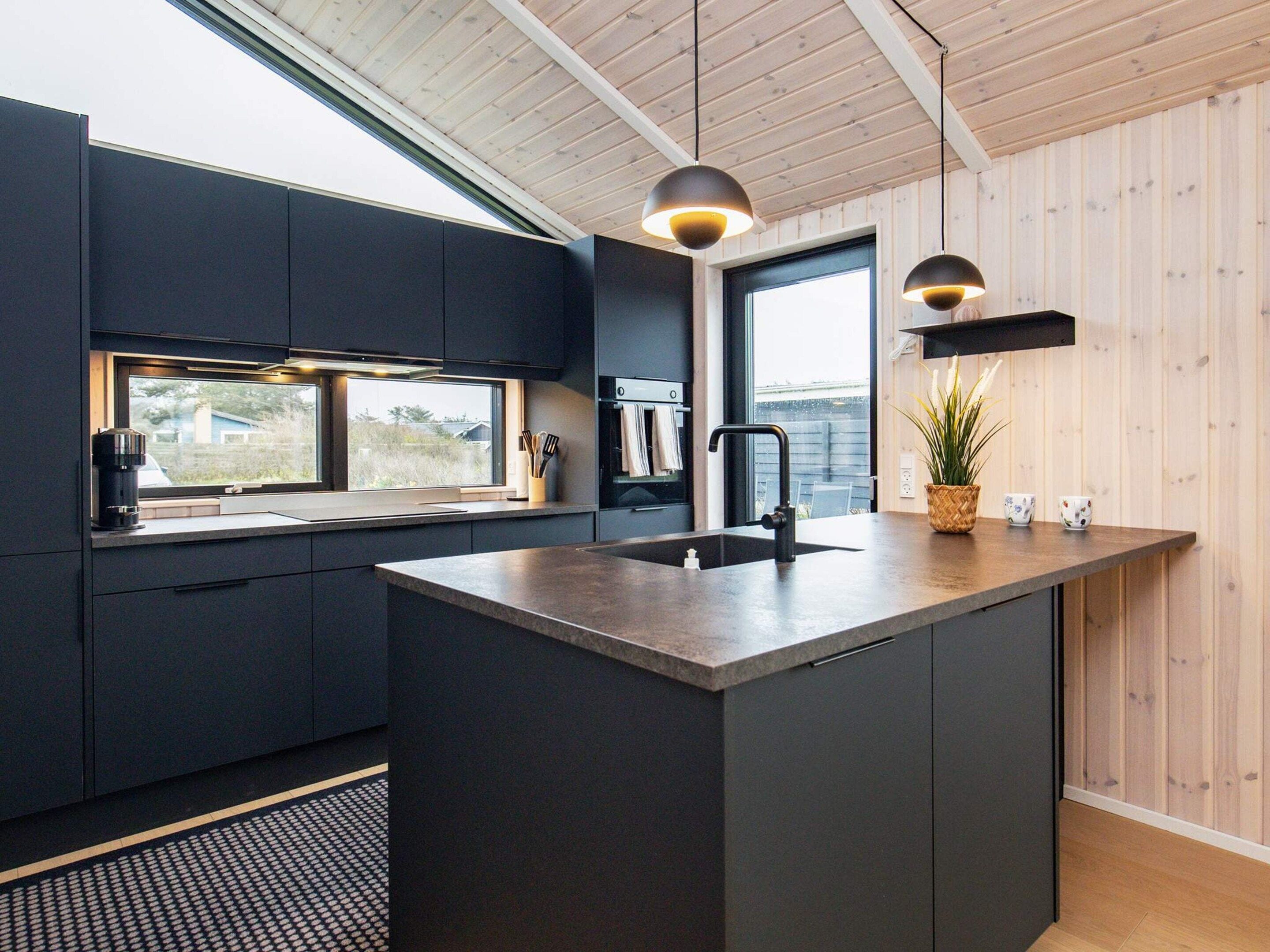 Une cuisine moderne avec des meubles de couleur sombre, un îlot central, une fenêtre offrant une belle vue et des luminaires suspendus.