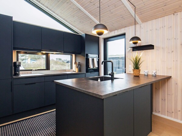 A modern kitchen with dark cabinetry, a central island, a window with a view, and pendant lighting.