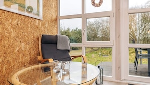 A cozy room with a glass table, a wicker chair, and a view of the outdoors through large windows. - Tranquil Nature Escape-by Traum (Thyholm)