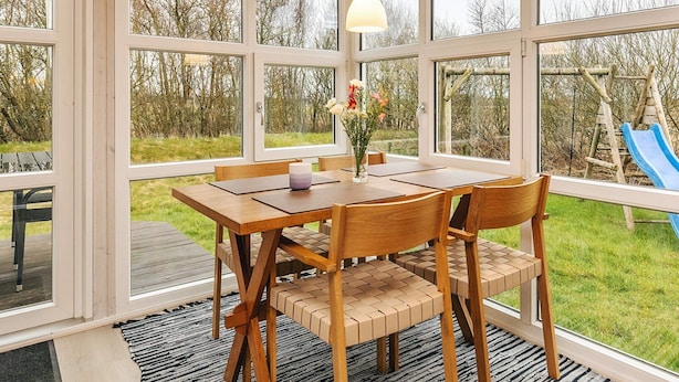 A sunroom with large windows, a wooden table, and chairs. - Tranquil Nature Escape-by Traum (Thyholm)