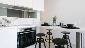 Uma cozinha moderna com armários brancos, forno embutido, exaustor de aço inoxidável e um espaço de bar com banquetas.
