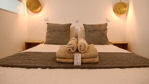 Cama bem arrumada com manta marrom, duas almofadas e uma toalha dobrada em cima. Há um aviso com uma mensagem na cama.