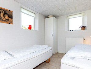 A small, clean room with two beds, a white wardrobe, and a window with a view of greenery outside.