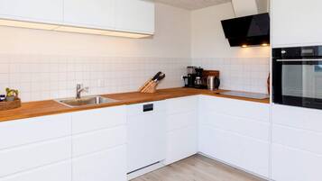 A modern kitchen with white cabinetry, a wooden countertop, a built-in dishwasher, and a black oven.