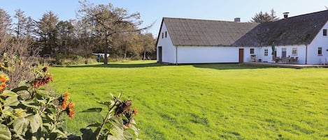 A white building with a sloped roof, surrounded by a well-maintained lawn and trees.