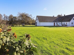 A white building with a sloped roof, surrounded by a well-maintained lawn and trees. - Holiday Home in HjÃ¸rring (Hjørring)