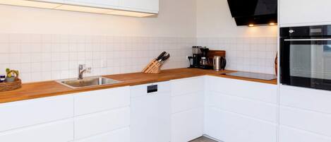 A modern kitchen with white cabinetry, a wooden countertop, a built-in dishwasher, and a black oven.