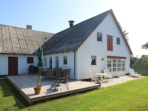 A white house with a sloped roof, a wooden deck, and outdoor seating.