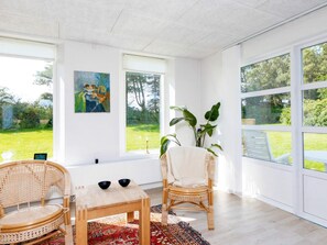 A bright room with large windows, a wooden table, two wicker chairs, and a colorful rug. - Holiday Home in HjÃ¸rring (Hjørring)