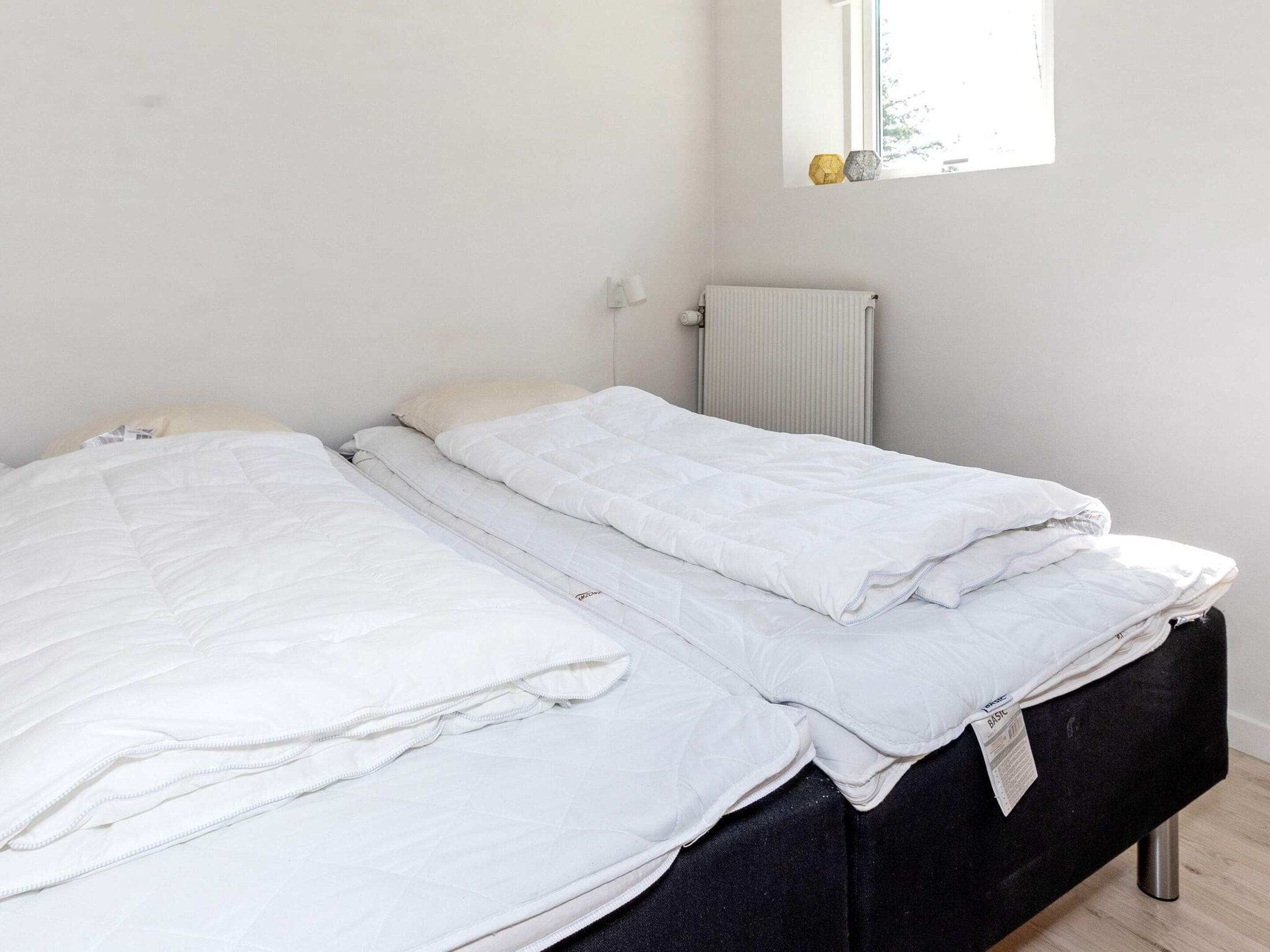 A bed with white bedding in a room with a radiator and a window with decorative items.