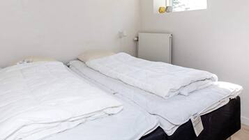 A bed with white bedding in a room with a radiator and a window with decorative items.