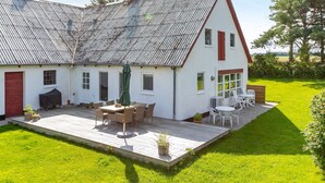 A two-story house with a sloped roof, a patio with outdoor furniture, and a well-maintained lawn.