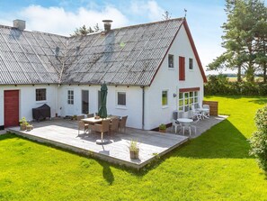 A two-story house with a sloped roof, a patio with outdoor furniture, and a well-maintained lawn.