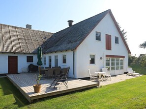 A white house with a sloped roof, a wooden deck, and outdoor seating.