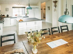 Una cocina moderna con armarios blancos, una isla central y un comedor con mesa y sillas de madera.