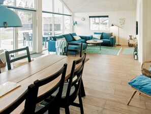 Amplia sala de estar con una mesa de comedor de madera, sofás azules y un ventanal que ofrece vistas al exterior.