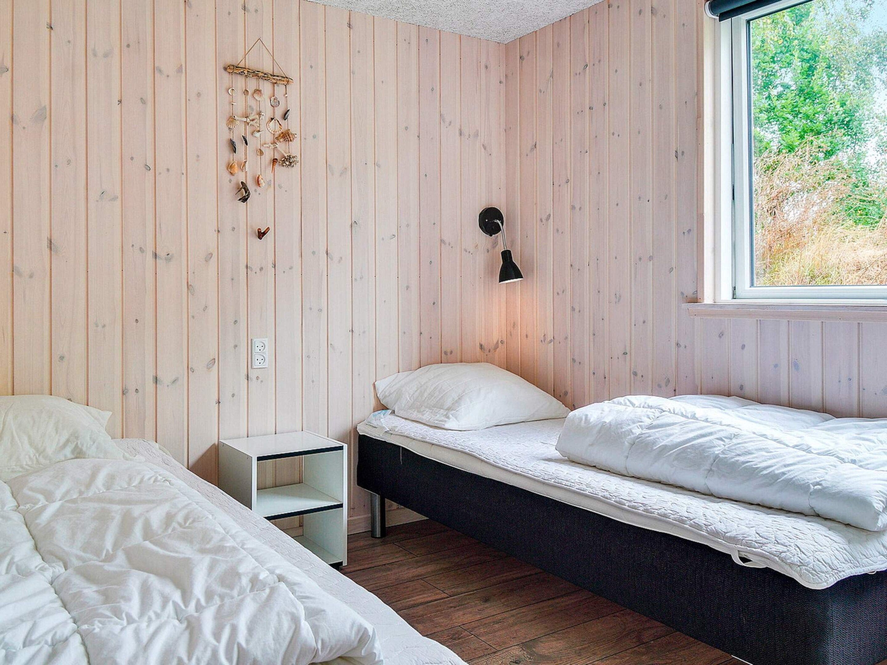 Ein Zimmer mit zwei Betten, einem Nachttisch, einer Wandleuchte und einem Fenster mit Blick auf Grünflächen.